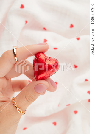 Female hand with pink gel polish manicure holding a red heart shaped chocolate candy Female hand with pink gel polish manicure holding a red heart shaped chocolate candy 108639768
