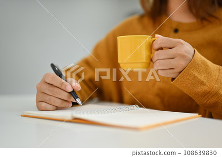 Young woman drinking hot coffee and writing notes in personal daily planner 108639830