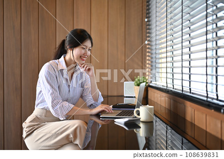 Attractive Asian female entrepreneur reading email on laptop computer at modern workplace Attractive Asian female entrepreneur reading email on laptop computer at modern workplace 108639831