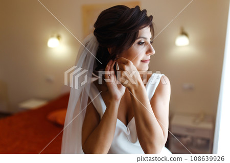 Morning of the bride. Beautiful smiling brunette bride in a white dress with a wedding bouquet in her hands. Morning of the bride. Beautiful smiling brunette bride in a white dress with a wedding bouquet in her hands. 108639926