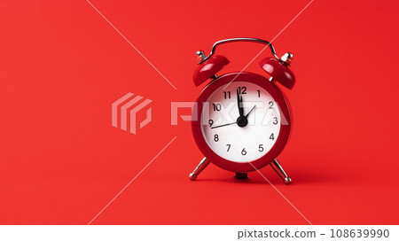 A classic red alarm clock stands out boldly against a monochromatic red background. 108639990