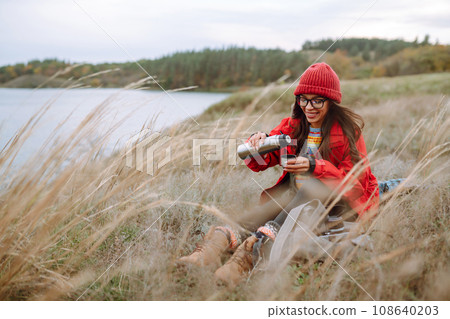Beautiful woman drinking tea from thermos on cold autumn day. Rest, relaxation, lifestyle concept. 108640203