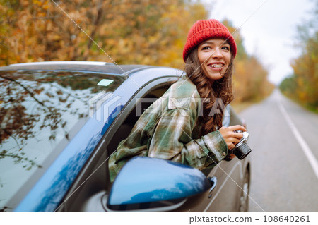 Beautiful woman takes pictures on camera from the car window. Smiling woman enjoying autumn weather. 108640261