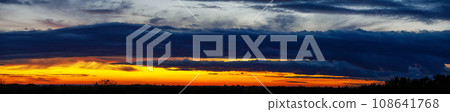Panoramic sunset sky with heavy dark blue clouds and orange line of sun 108641768