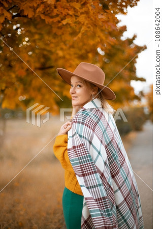autumn woman in a green dress, brown hat, plaid, against the background of an autumn tree 108642004