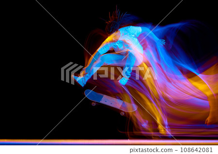 Full-length portrait of man dressed modern stylishly outfit skateboarding with neon flashes of light isolated black background. Full-length portrait of man dressed modern stylishly outfit skateboarding with neon flashes of light isolated black background. 108642081
