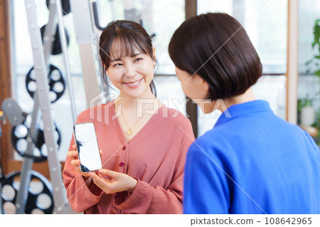顧客向健身房工作人員展示智慧型手機螢幕 顧客向健身房工作人員展示智慧型手機螢幕 108642965