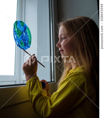 Cute little girl painting planet on window at home. Happy Earth Day April 22 greeting message.Creative family leisure 108643049