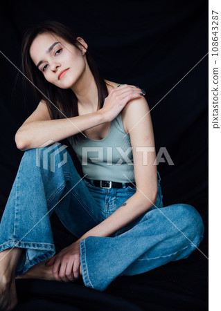 a woman in denim pants sits on a chair on a black background a woman in denim pants sits on a chair on a black background 108643287