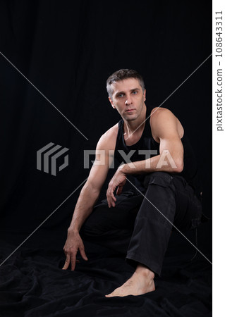 a man in dark clothes sits in a dark room 108643311