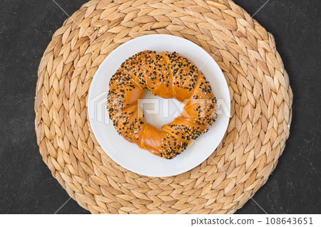 Turkish bagel simit with sesames on white plate and wicker napkin on black background. Top view 108643651