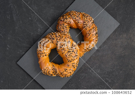 Tasty fresh toasted bagels sprinkled with white and black sesame seeds on a dark background. Turkish bagels or simits - traditional bakery. Top view, copy space Tasty fresh toasted bagels sprinkled with white and black sesame seeds on a dark background. Turkish bagels or simits - traditional bakery. Top view, copy space 108643652