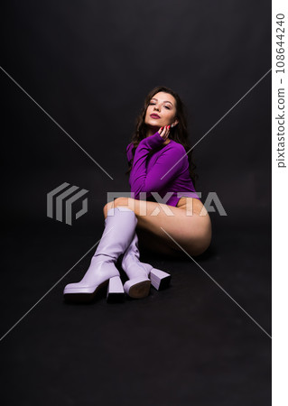 Seductive young female in violet bodysuit on dark and red background 108644240