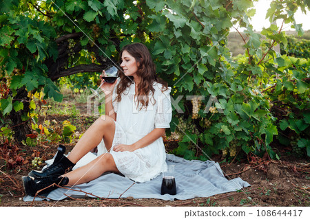 A woman under a vineyard drinks wine from a glass 108644417