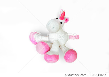 Pink soft unicorn toy sitting at white background. Isolated studio image 108644654