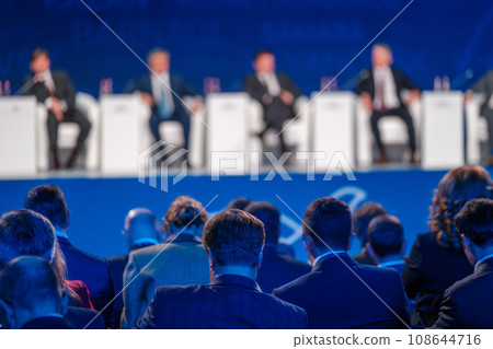 Male business professionals listening to board of directors on stage during conference meeting at export forum  108644716