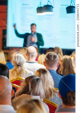 Back view of multiethnic business professionals listening to speaker giving presentation in conference hall Back view of multiethnic business professionals listening to speaker giving presentation in conference hall 108644731