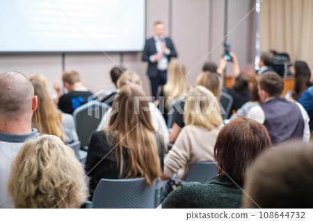 Back view of businesswoman attending presentation with diverse participants in conference hall  108644732