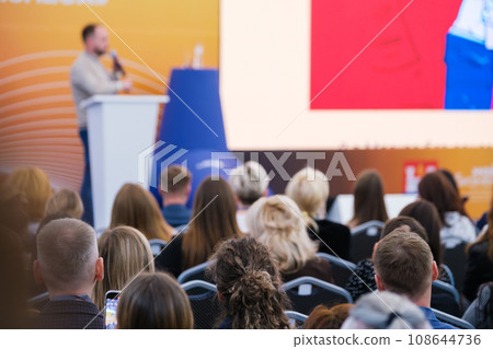 Multiracial businesspeople listening to speaker behind podium during global workshop at conference hall Multiracial businesspeople listening to speaker behind podium during global workshop at conference hall 108644736
