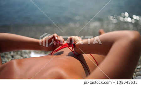 Woman taking red bikini off on beach for tan, lady stripping