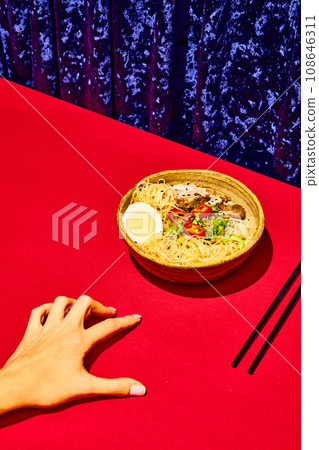 Asian culture, cuisine. Japanese soba in clay bowl. Hand reaches for plate with tasty noodles, egg and meet, served with greenery. 108646311