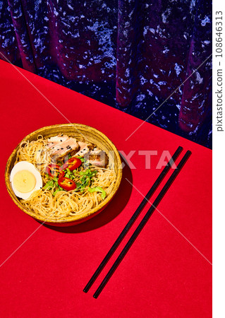 Asian culture, cuisine. Japanese soba in clay bowl. Plate with noodles, egg and meet, served with greenery isolated red background. 108646313