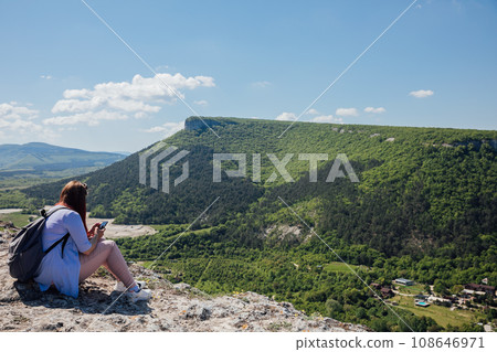 a woman sitting with a phone on a mountain hiking journey nature 108646971