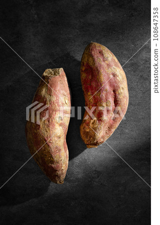 Old sweet potatoes placed on a black slate board. 108647358