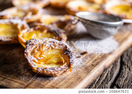 Mini tarts made of puff pastry and sliced apples sprinkled with powdered sugar on wooden cutting board 108647631