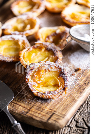 Mini tarts made of puff pastry and sliced apples sprinkled with powdered sugar on wooden cutting board Mini tarts made of puff pastry and sliced apples sprinkled with powdered sugar on wooden cutting board 108647632