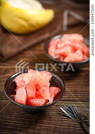 Grapefruits with red flesh placed on a wooden board in a bowl. 108647695
