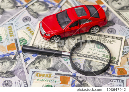 Magnifying glass and toy red car on dollar bills background Magnifying glass and toy red car on dollar bills background 108647942