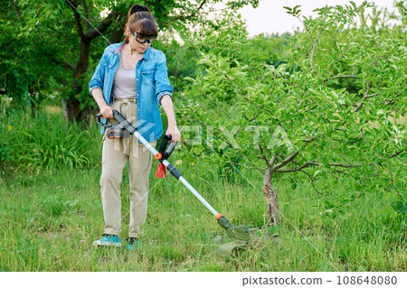 Woman mowing grass with cordless trimmer in garden 108648080