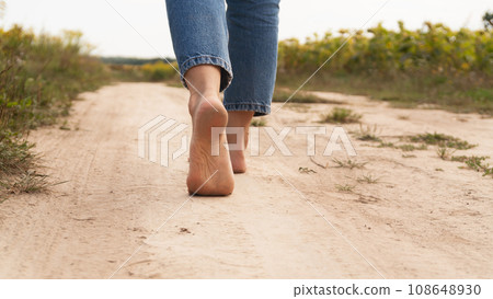 Woman walking in field meadow. Close-up of bare feet soiled with the ground. Woman walking in field meadow. Close-up of bare feet soiled with the ground. 108648930