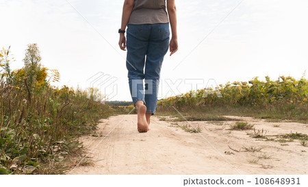 Woman walking in field meadow. Close-up of bare feet soiled with the ground. 108648931