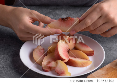 Authentic female hands holding a piece of a fresh cutting ripe peach on white plate 108652108