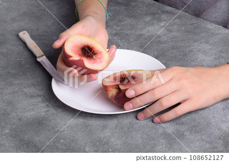 Authentic female hands holding a two half of a fresh ripe peach on white plate on a grey table 108652127