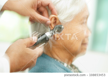 Otolaryngologist or ENT physician doctor examining senior patient ear with otoscope, hearing loss problem. Otolaryngologist or ENT physician doctor examining senior patient ear with otoscope, hearing loss problem. 108653453