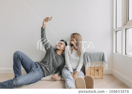 Happy and relax couple sit on the floor using and watch mobile. 108653878