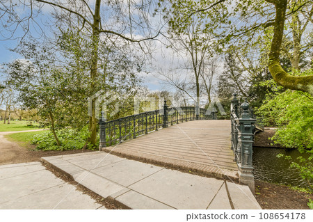 a bridge in the middle of a park with some trees and bushes on either side of the path that leads up to it 108654178
