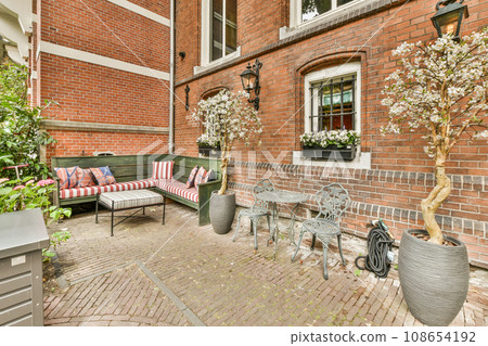 an outside area with furniture and flowers on the side of a brick building, in front of a green bench an outside area with furniture and flowers on the side of a brick building, in front of a green bench 108654192