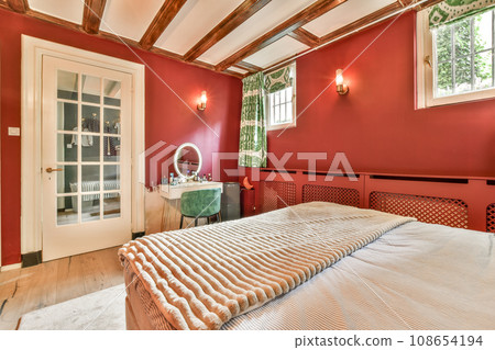 a bed in a room with red walls and wood beams on the ceiling, there is a mirror hanging above it a bed in a room with red walls and wood beams on the ceiling, there is a mirror hanging above it 108654194