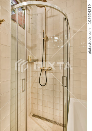 a bathroom with a glass shower door and tiled walls in the corner to the left is a white bathtub on the right side 108654219