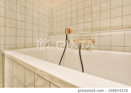 a bathtub in a bathroom with white tiles on the walls, and a black shower hose attached to the tub 108654220