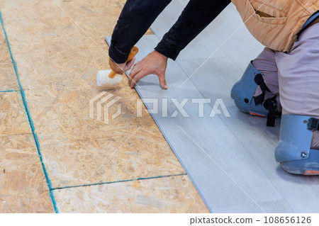 An installation worker installs vinyl laminate flooring in new home 108656126