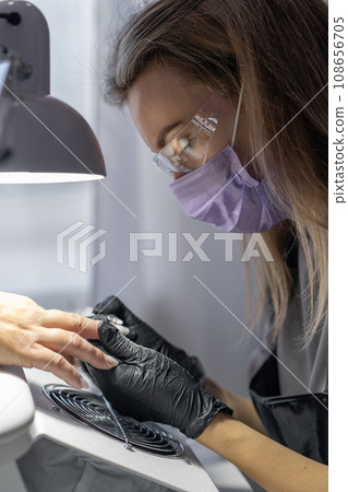Manicurist at work. Professional manicurist removes old worn nail design from nails of client using modern electric drill. Preparing fingernails for making fresh manicure and applying new nail design 108656705
