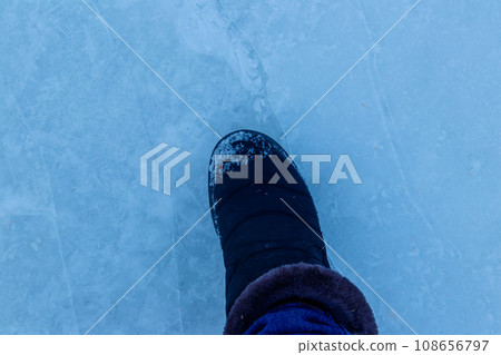 Foot standing on cracked natural lake ice texture. Concept of danger exit to badly frozen water 108656797