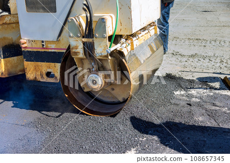 As asphalt is being laid on new road worker uses an asphalt roller compactor As asphalt is being laid on new road worker uses an asphalt roller compactor 108657345