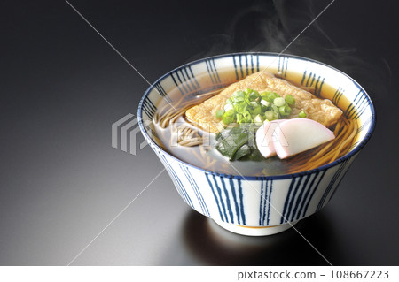 Hot fox soba with fried tofu, kamaboko, wakame, and green onion photographed against a black background Hot fox soba with fried tofu, kamaboko, wakame, and green onion photographed against a black background 108667223