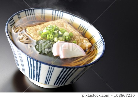 黑色背景下拍攝的熱狐蕎麥麵,配上炸豆腐、魚糕、裙帶菜和蔥 黑色背景下拍攝的熱狐蕎麥麵,配上炸豆腐、魚糕、裙帶菜和蔥 108667230